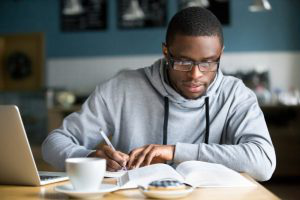 Focused millennial african student making notes while studying in cafe